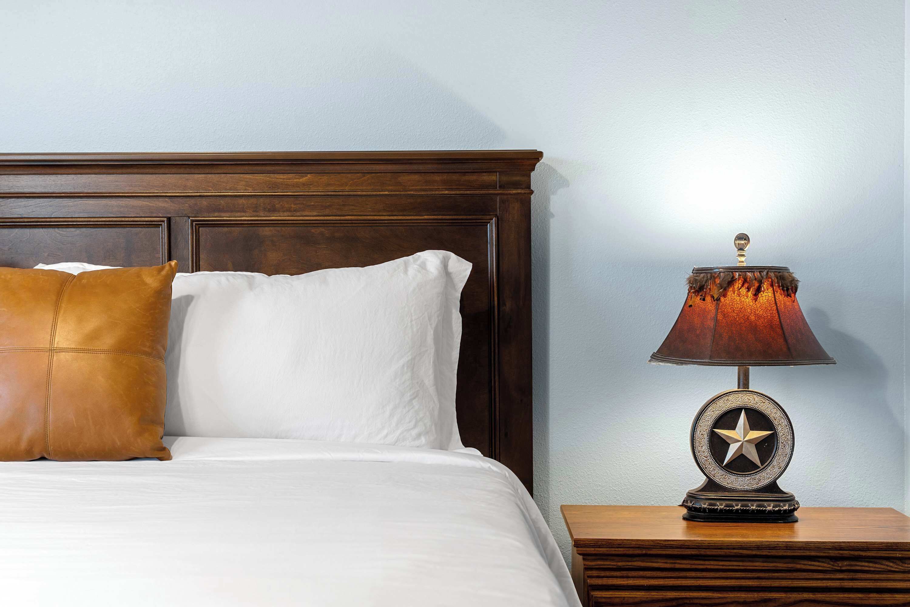 A neatly made bed with white and brown pillows, a wooden nightstand with a lamp, and a wall with a textured pattern.