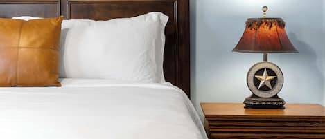 A neatly made bed with white and brown pillows, a wooden nightstand with a lamp, and a wall with a textured pattern.