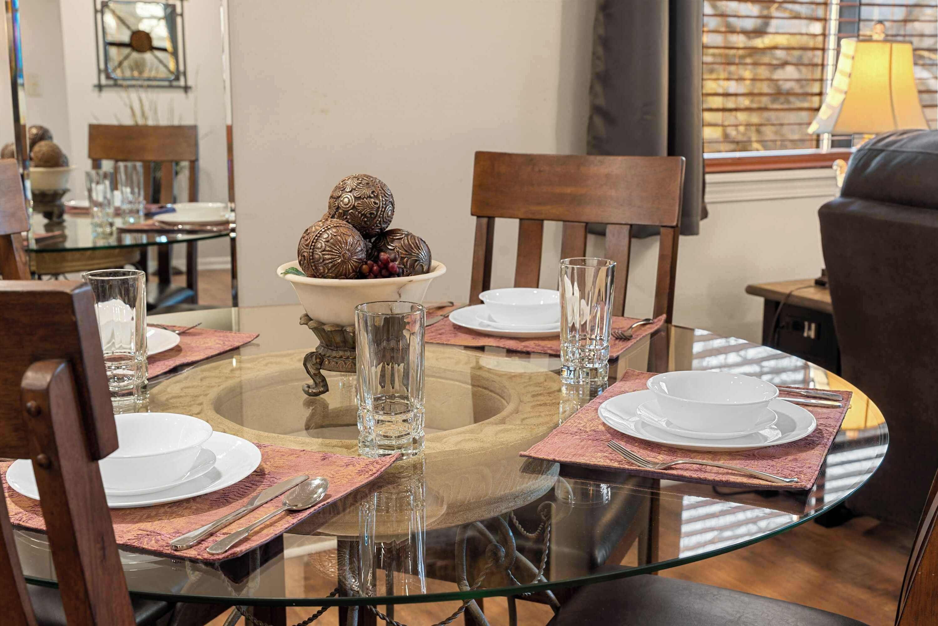 A dining area with a round glass table set for four, surrounded by wooden chairs.