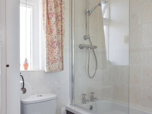 A bathroom with a toilet, a shower with a glass door, and a window with a floral curtain.