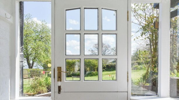 Eine weiße Tür mit sechs Fenstern, einer kleinen Sitzbank und Blick auf einen Garten.
