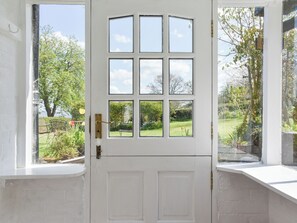 A white door with six windows, a small window seat, and a view of a garden.