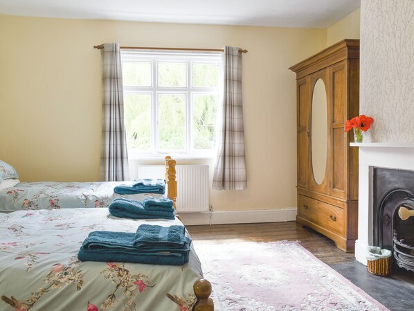 A bedroom with a bed, a radiator, a window with curtains, a wooden wardrobe, and a fireplace.