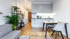 Une cuisine moderne avec des meubles blancs, un coin repas comprenant une table et des chaises, et un canapé gris.