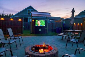A backyard with a fire pit, outdoor seating, and a TV screen.