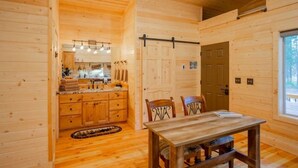 A wooden cabin interior with a dining area, kitchen, and a large window. - Tiny Timber-28 miles to Yellowstone (Island Park)