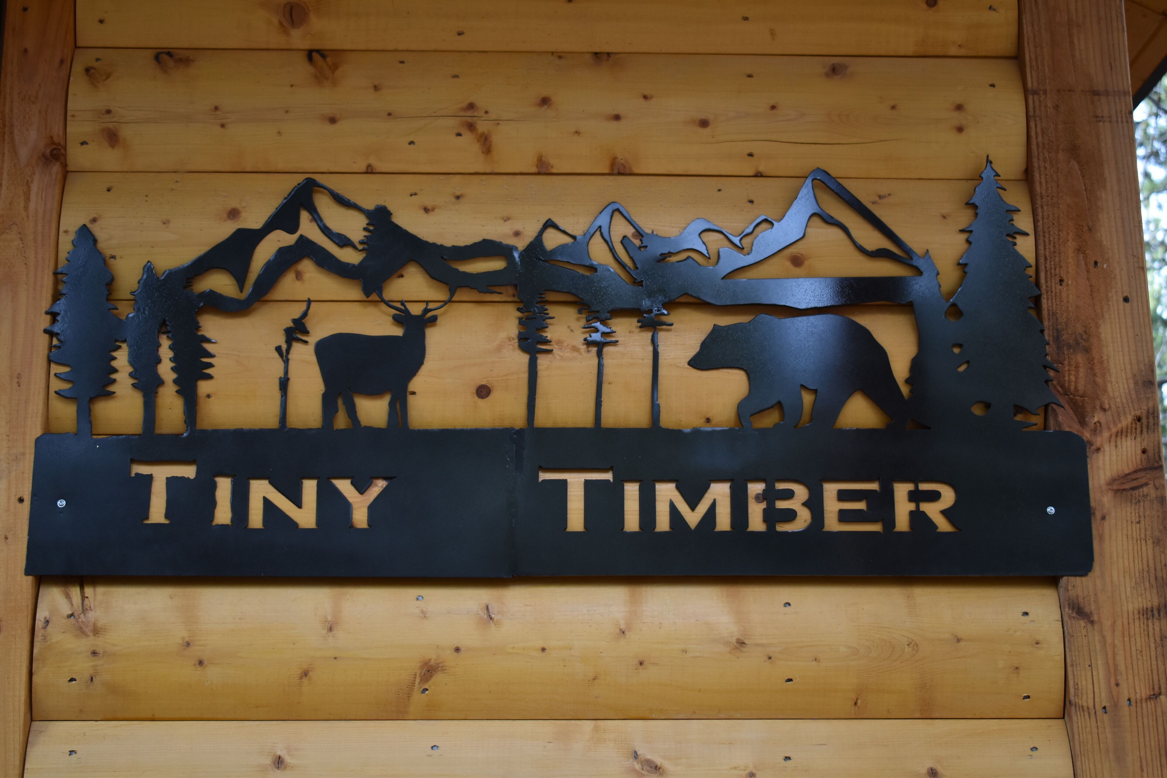 A wooden sign with silhouettes of mountains, trees, and animals, and the words "TINY TIMBER" on it.