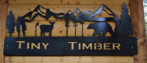 A wooden sign with silhouettes of mountains, trees, and animals, and the words "TINY TIMBER" on it.