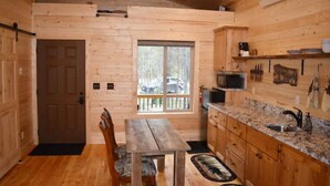 A wooden cabin interior with a dining area, kitchen, and a large window. - Tiny Timber-28 miles to Yellowstone (Island Park)