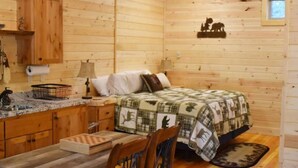 A cozy log cabin room with a wooden bed, a small desk, a chair, and a window with a view of the outdoors. - Tiny Timber-28 miles to Yellowstone (Island Park)