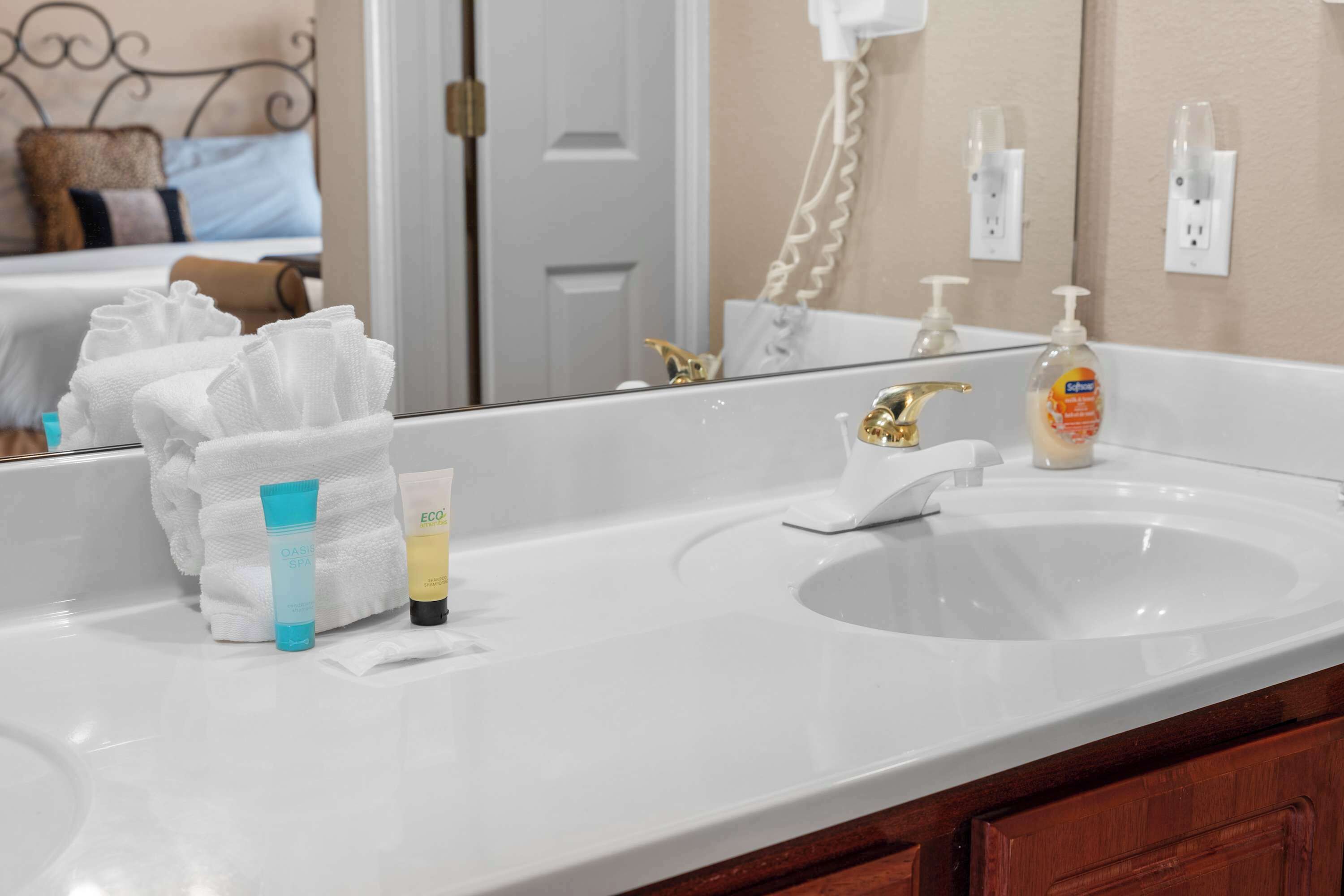 A hotel bathroom with a white sink, a mirror, and toiletries on the counter.