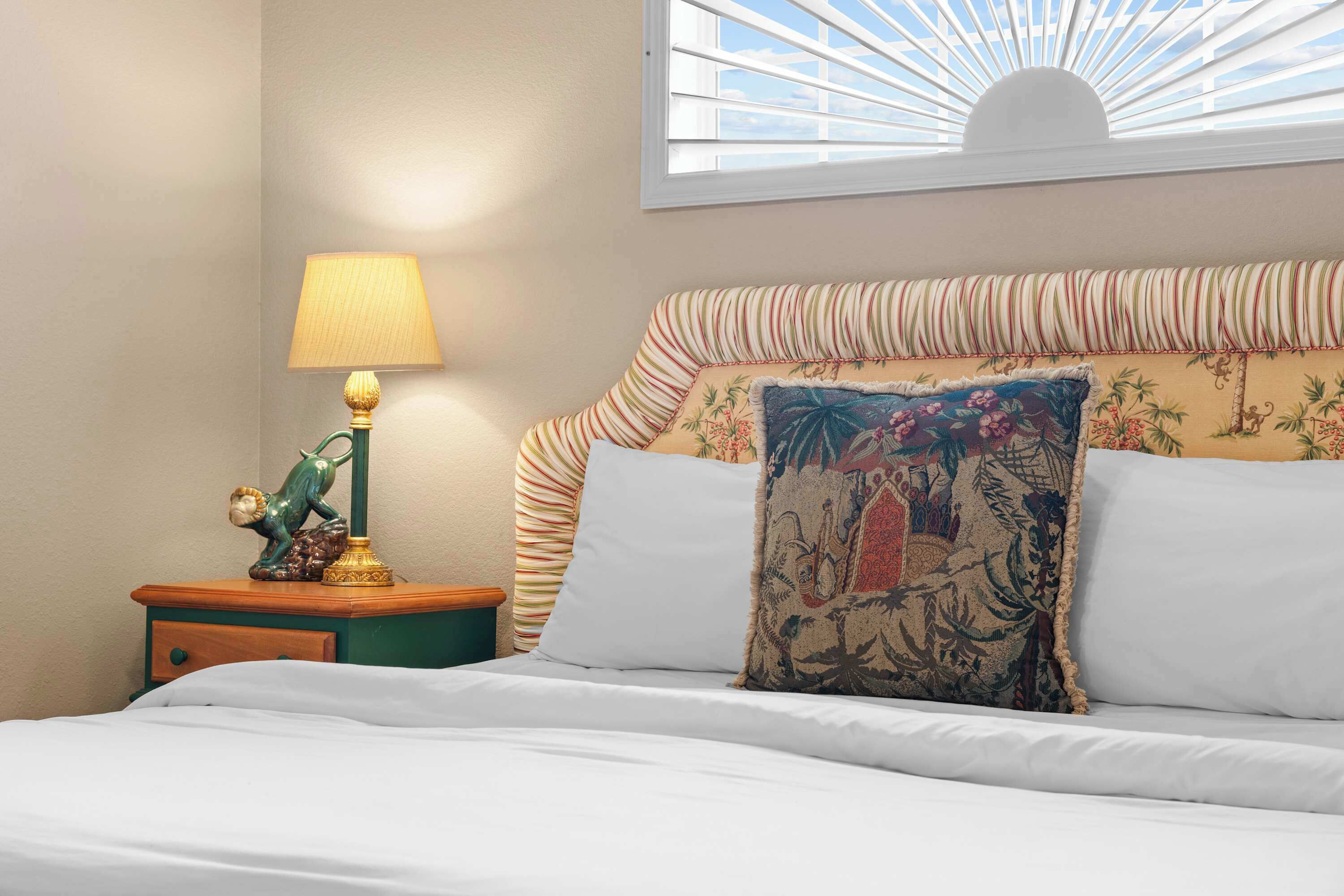 A bed with white bedding, a striped pillow, and a decorative pillow with a tropical design.
