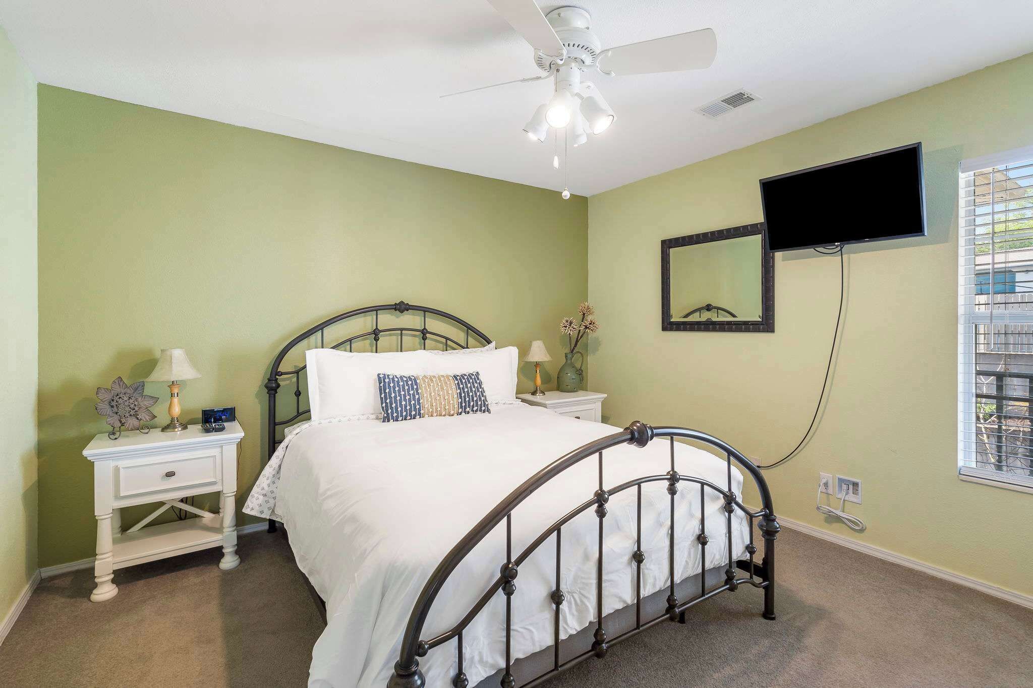 A bedroom with a bed, nightstands, a ceiling fan, a TV, and a window.
