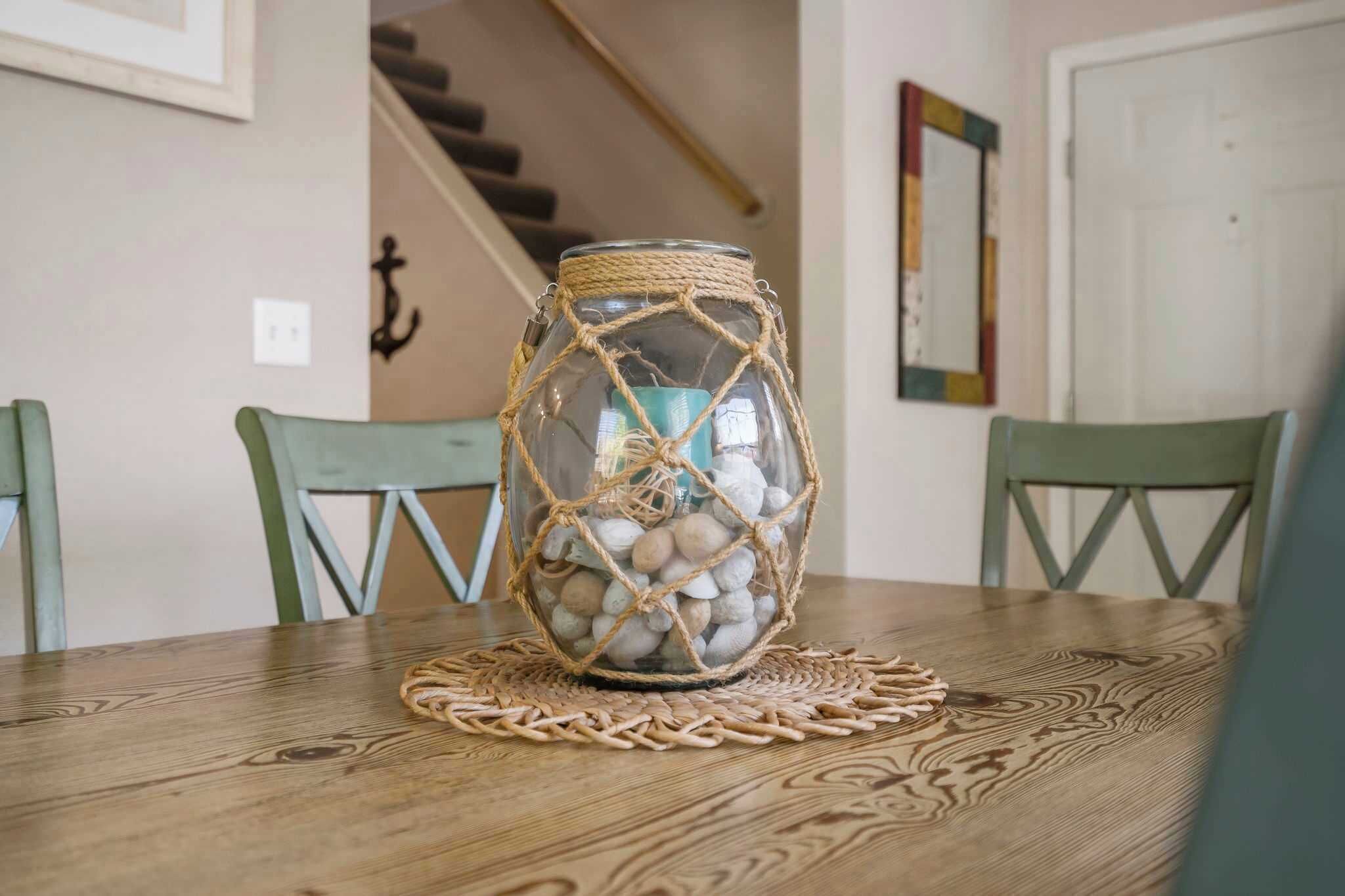 A glass jar filled with pebbles, wrapped in twine, placed on a wooden table with a woven placemat.