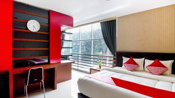 A modern hotel room with a large bed, a desk, a chair, a TV, and a window with a view of greenery.