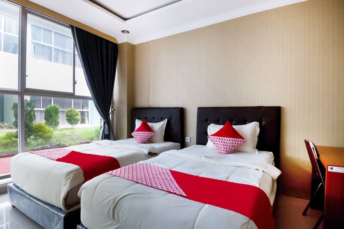 A hotel room with two beds, a large window, and a view of greenery outside.