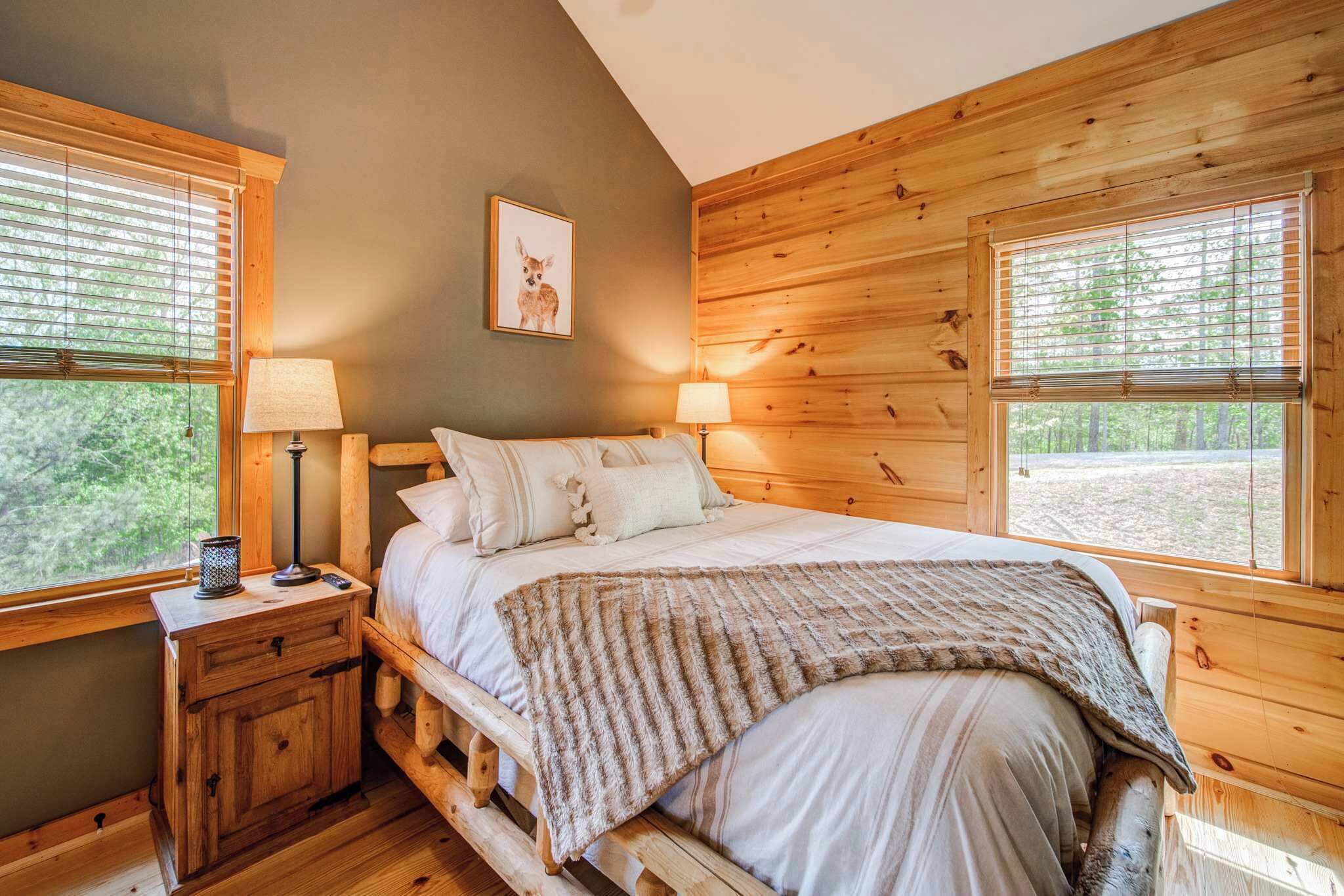 A wooden cabin bedroom with a bed, two bedside tables, lamps, and a framed picture on the wall.