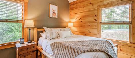 A wooden cabin bedroom with a bed, two bedside tables, lamps, and a framed picture on the wall.