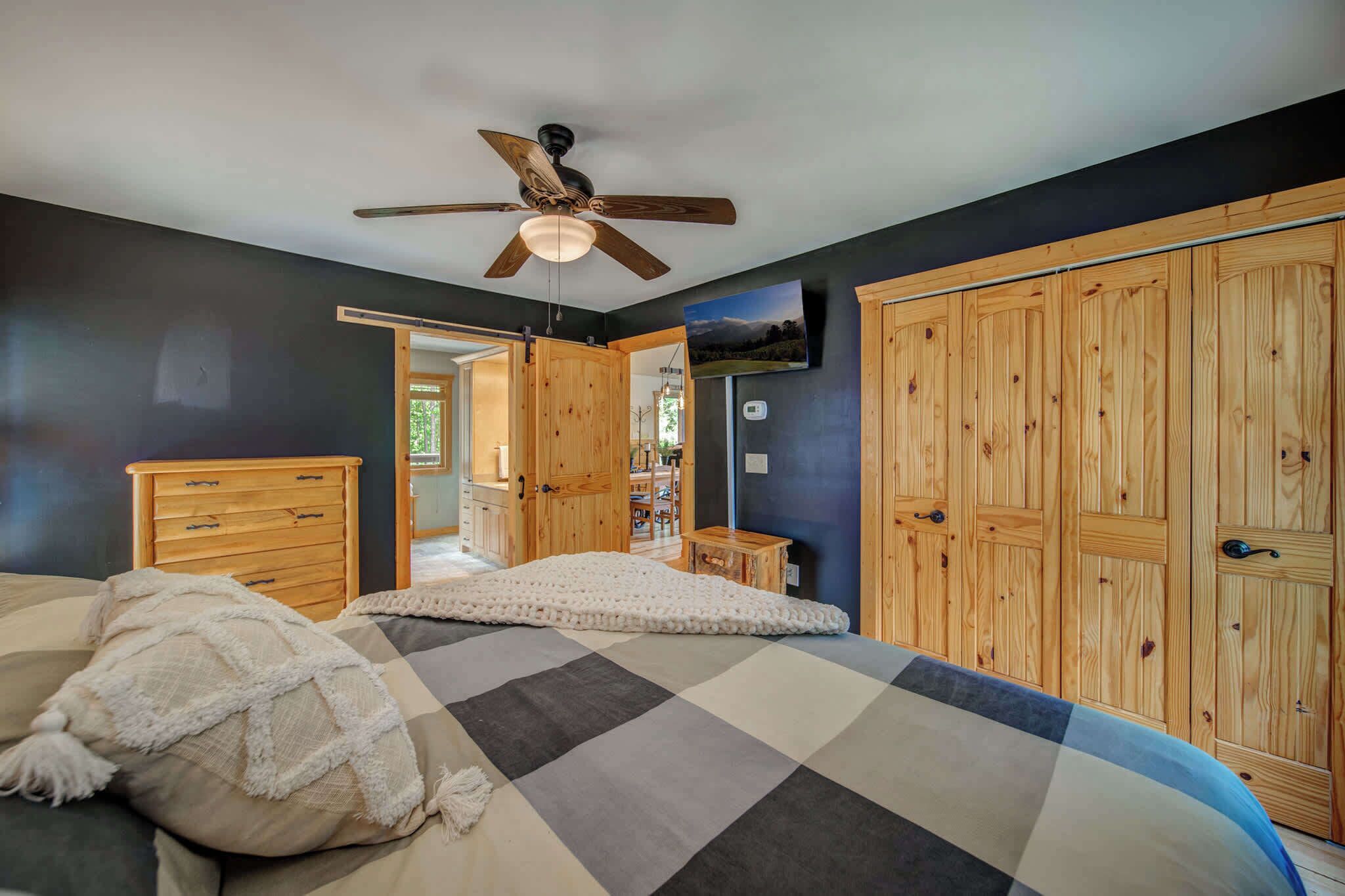 A bedroom with a bed, wooden wardrobe, ceiling fan, and a view of the hallway.