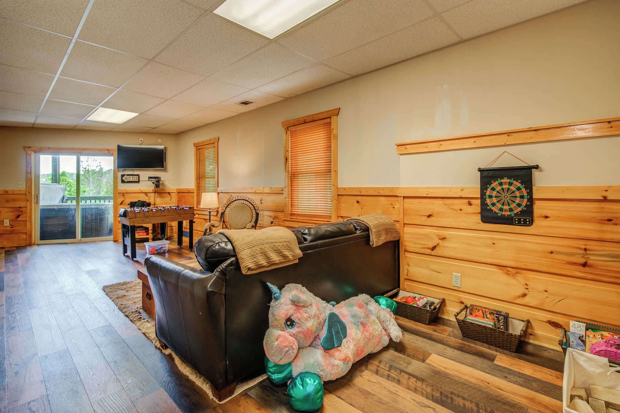 A cozy room with a leather couch, a dartboard, and a television on the wall.