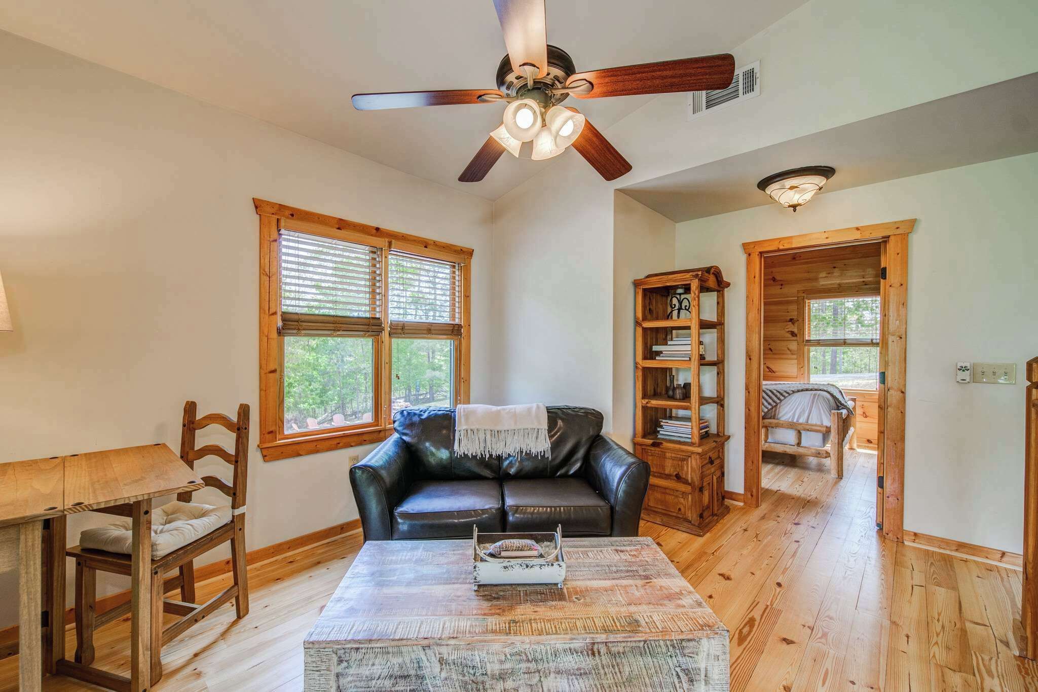 A spacious living room with a black leather sofa, wooden coffee table, and a ceiling fan.