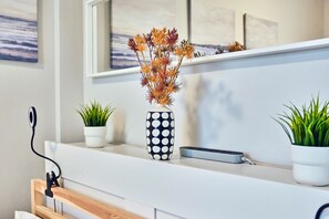 A modern bathroom with a white countertop, a black and white polka dot vase with dried flowers, and two potted plants.