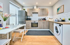 A modern kitchen with wooden cabinets, a stainless steel refrigerator, a microwave, an oven, and a washing machine.