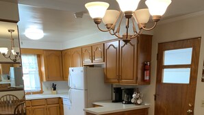 A kitchen with wooden cabinets, a white refrigerator, a coffee maker, and a dining table with chairs. - Family Home, Blocks from Pro Football Hall of Fame, Fenced Yard, Pet Friendly (Canton)