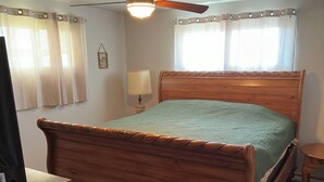 A bedroom with a wooden bed, a ceiling fan, a bedside lamp, and a window with curtains. - Family Home, Blocks from Pro Football Hall of Fame, Fenced Yard, Pet Friendly (Canton)
