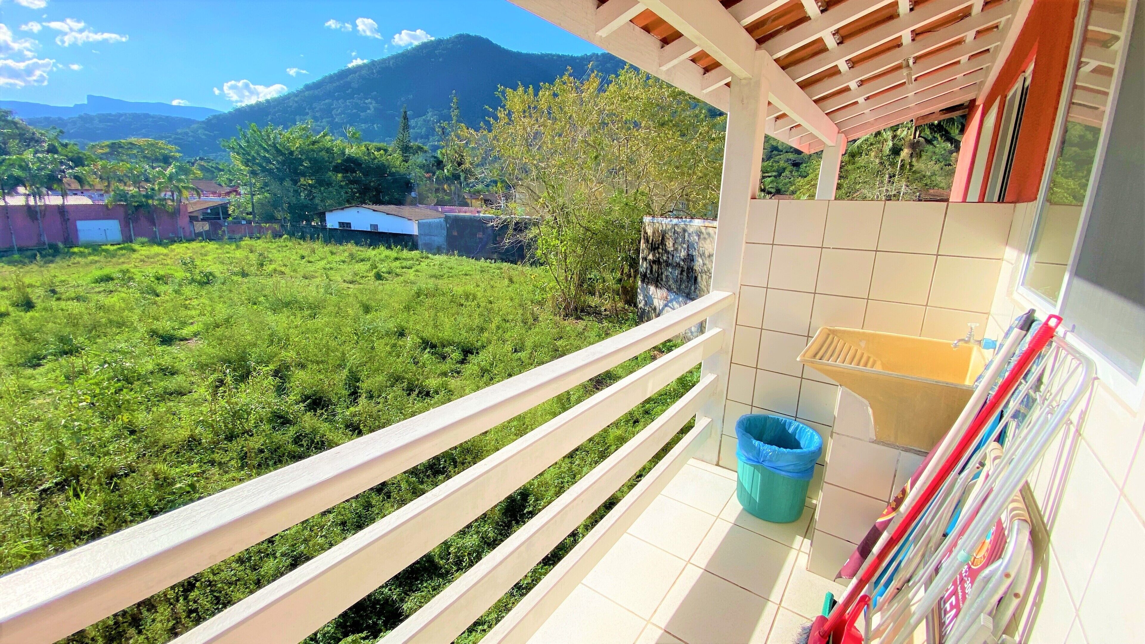 A balcony with a view of a lush green landscape, a tiled wall, and a metal rack with cleaning supplies.