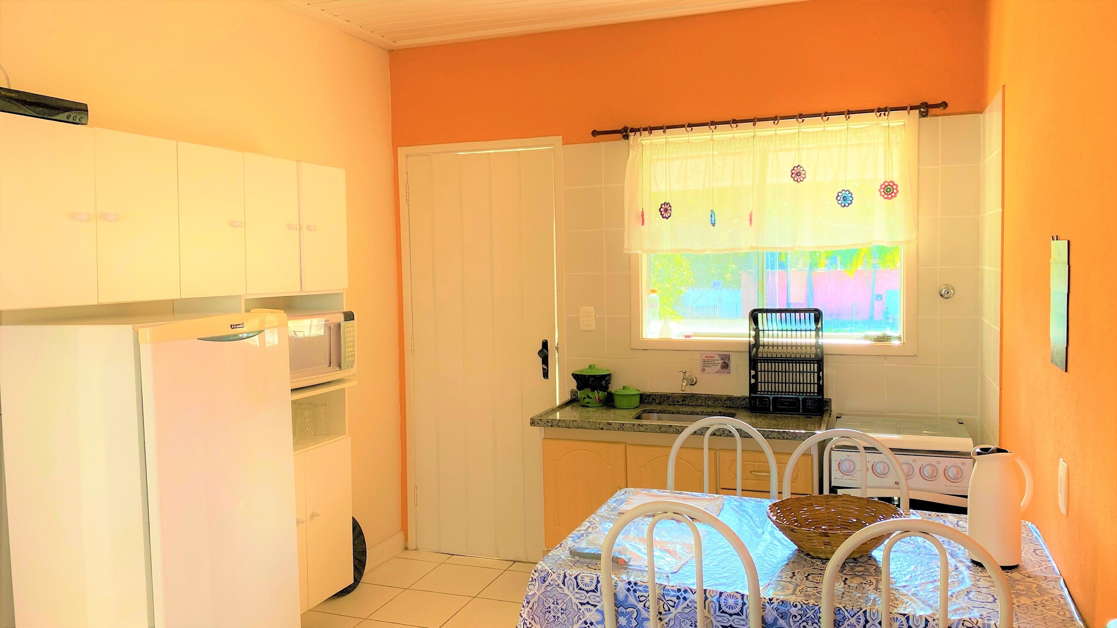 A compact kitchen with white cabinets, a refrigerator, a microwave, and a window with a floral curtain.