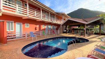 A pool area with a red building, outdoor seating, and a mountain in the background.