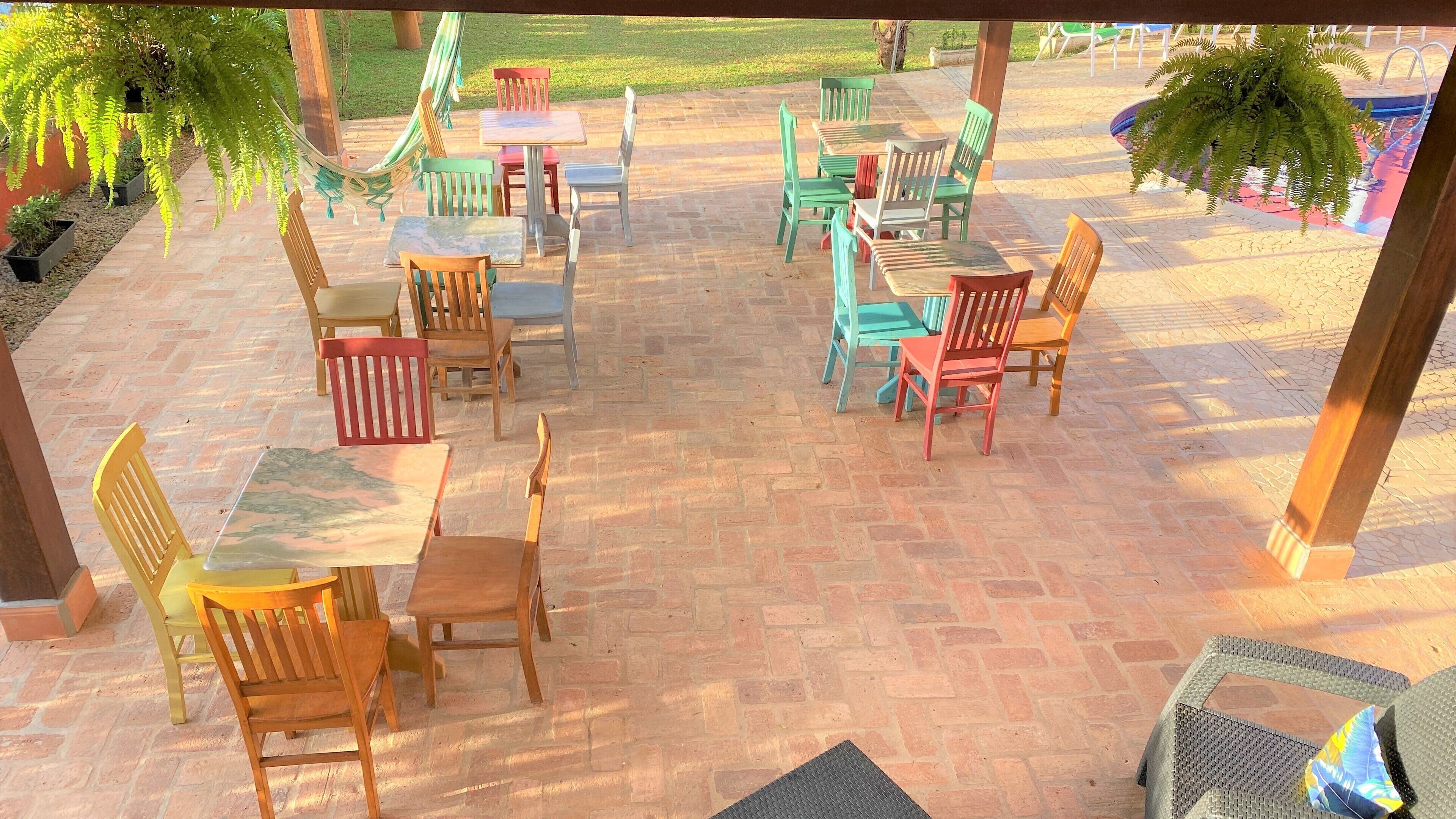 An outdoor patio area with multiple wooden and plastic chairs and tables, arranged on a brick floor.