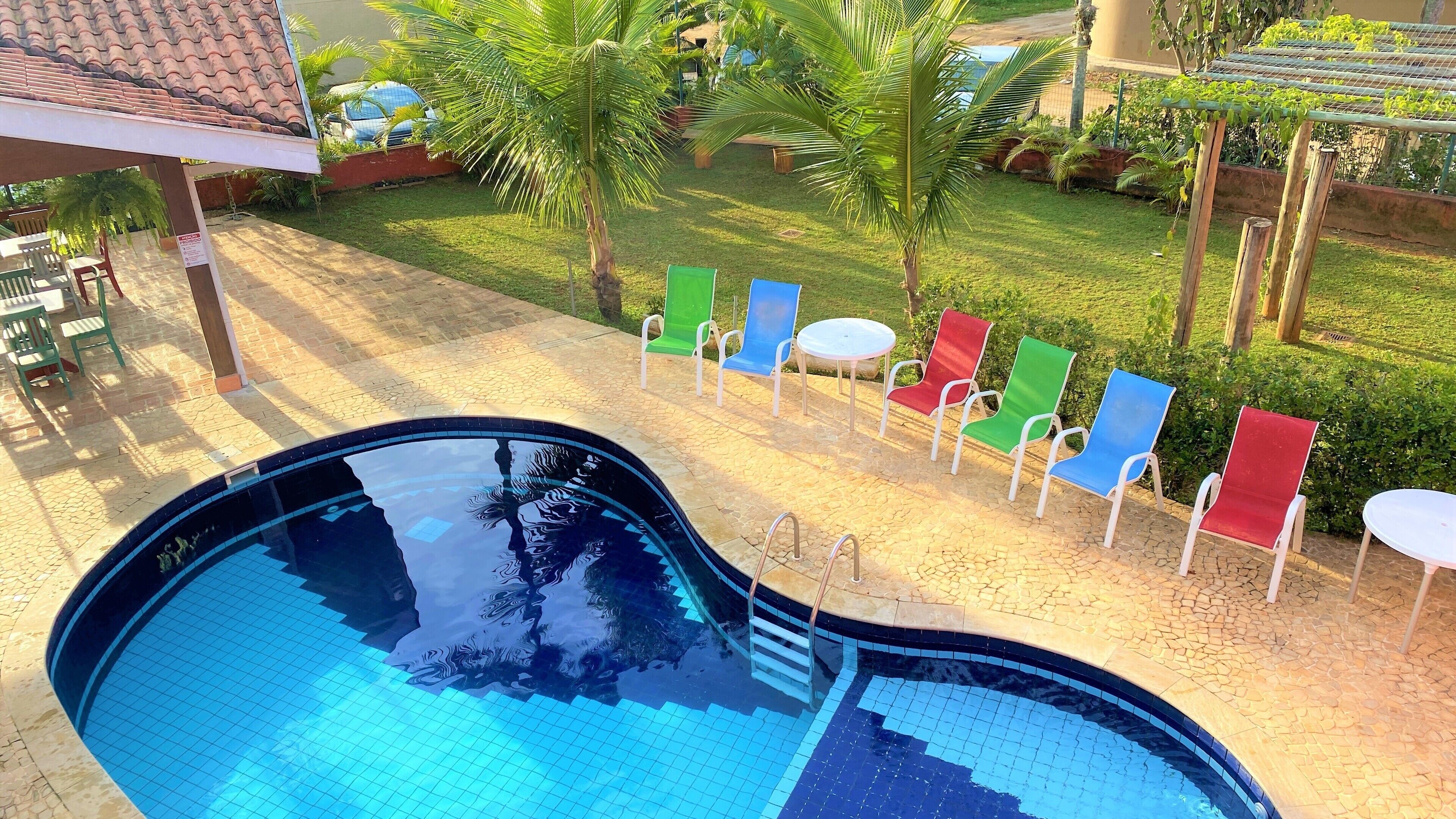 A swimming pool with a tiled deck, surrounded by colorful lounge chairs and a grassy area with palm trees.
