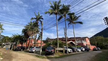 Una calle residencial con coches aparcados, palmeras y un edificio rojo con un cartel que dice 'Pousada De Bem K Vida'.