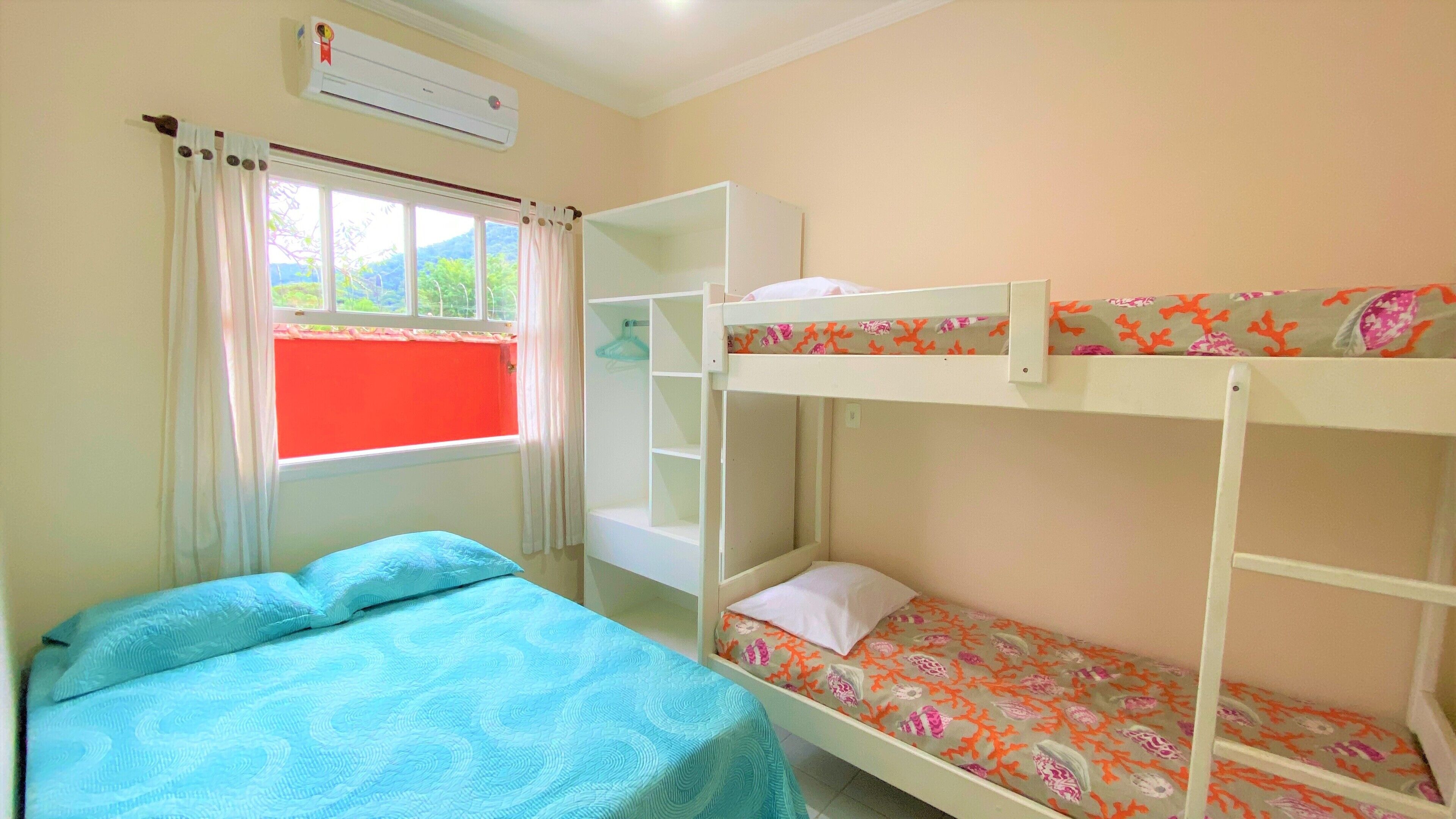 A bunk bed room with a window, a bed with a blue bedspread, and an air conditioning unit.