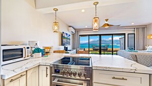 A modern kitchen with a built-in stove, oven, and microwave. It features a large island with a marble countertop and a view of the ocean through large sliding glass doors.