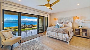 A bedroom with a large bed, a ceiling fan, a nightstand, and a view of the ocean.