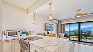 A modern kitchen with a marble countertop, stainless steel appliances, and pendant lighting.