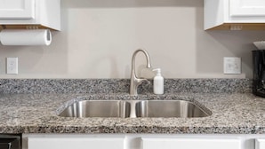 A kitchen with a granite countertop, stainless steel sink, and white cabinets. - Country Farmhouse - Best of Branson! (Branson)
