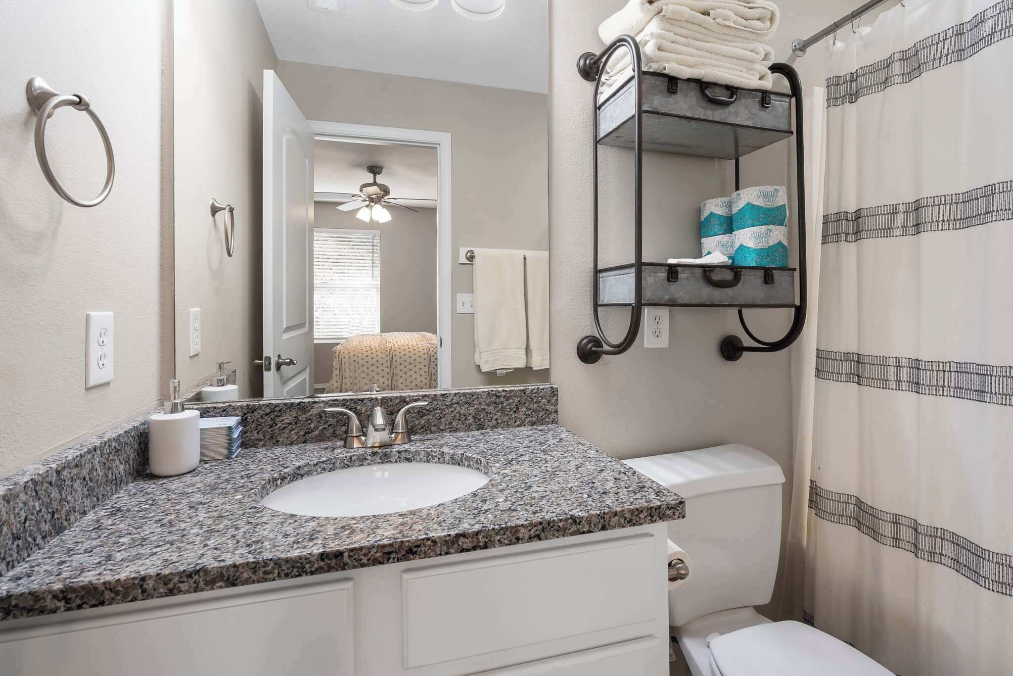 A bathroom with a granite countertop sink, a toilet, a towel rack, and a shower curtain.