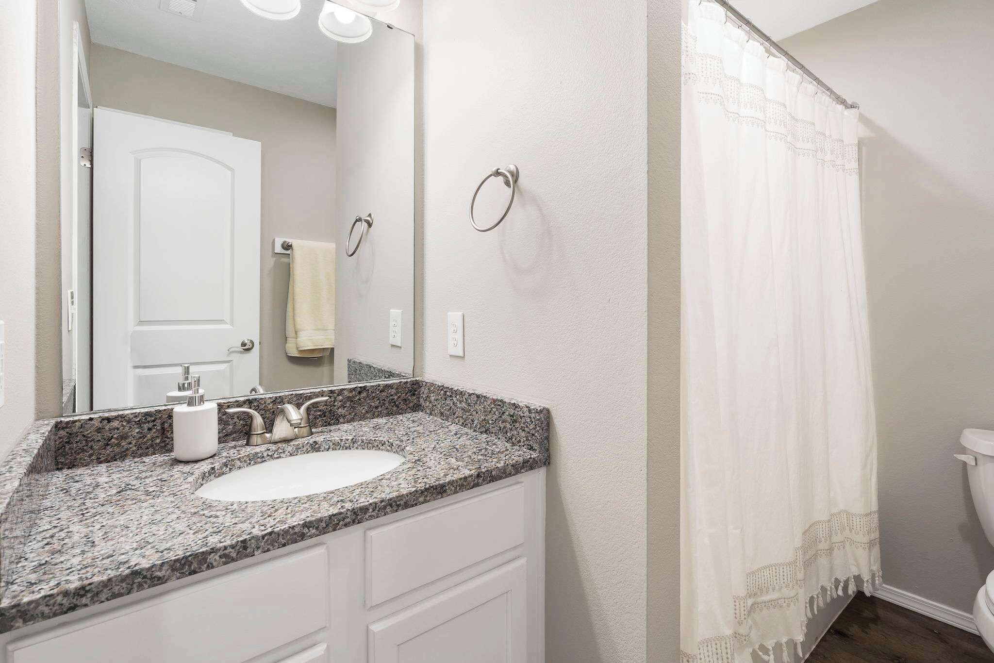 A bathroom with a granite countertop sink, a mirror, a towel ring, and a shower curtain.