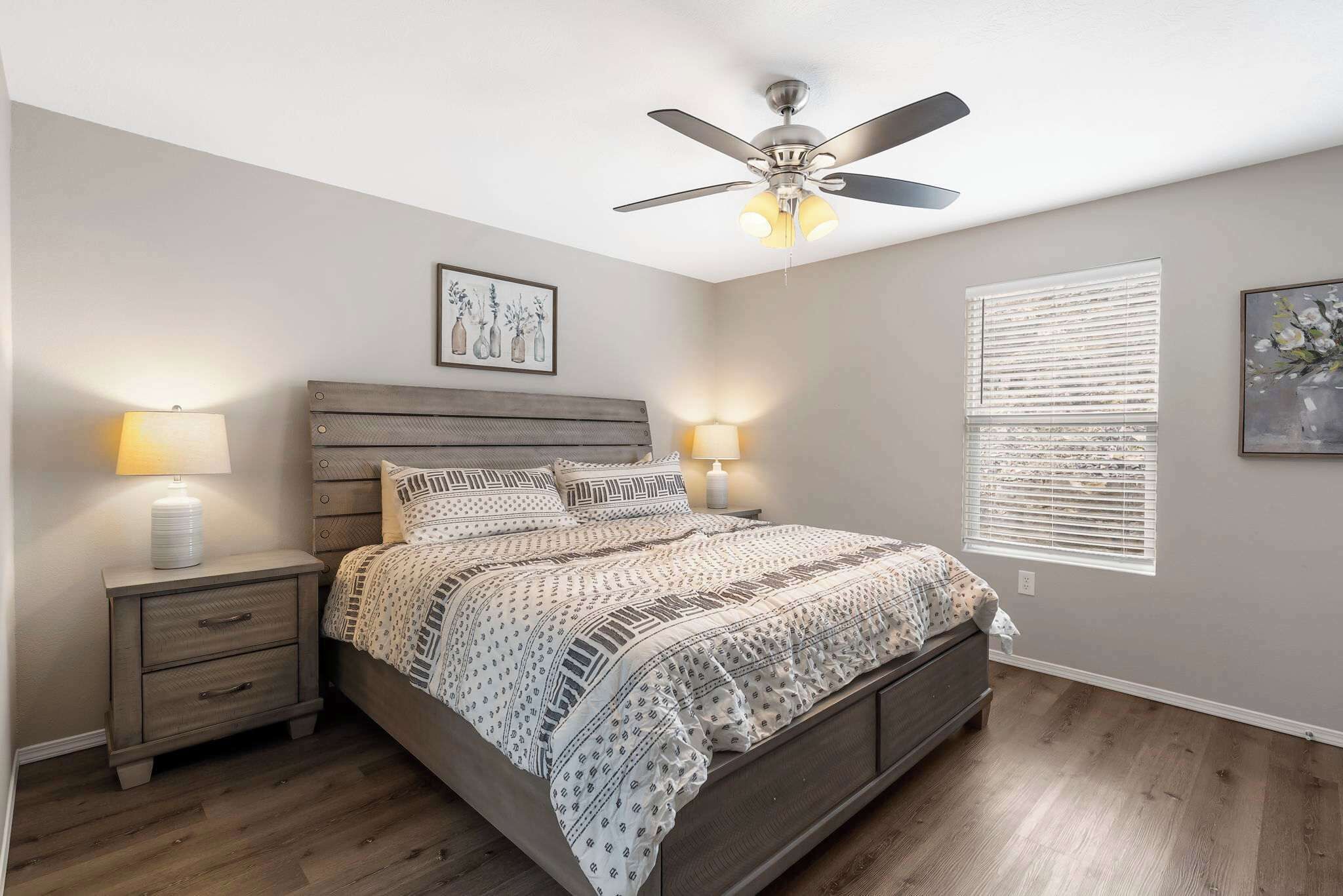 A bedroom with a bed, nightstands, a ceiling fan, and wall-mounted artwork.