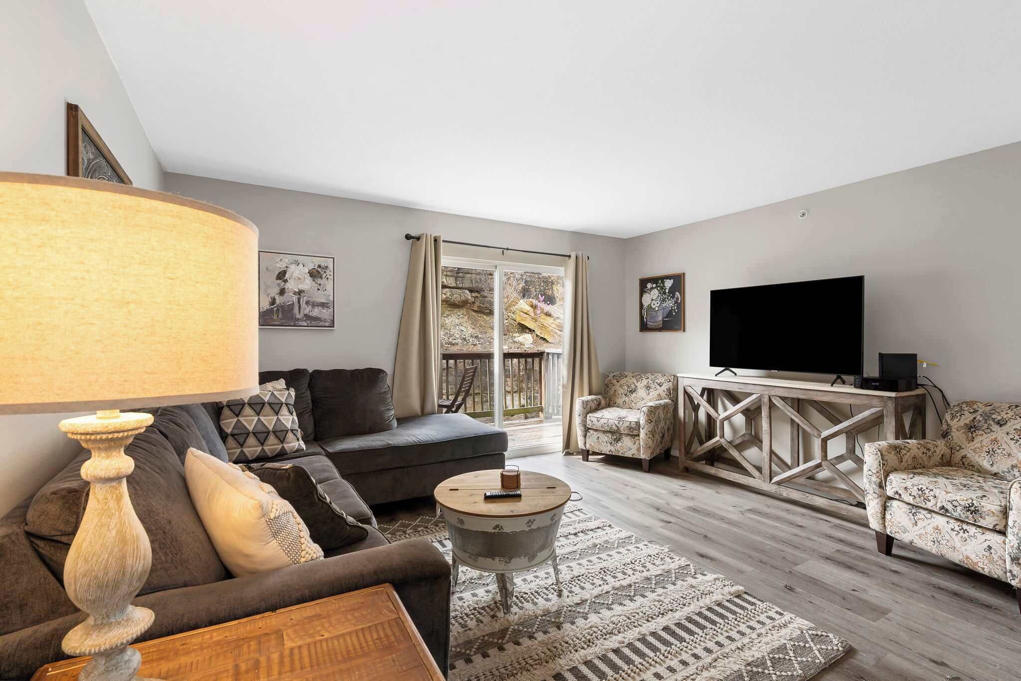 A living room with a sofa, armchairs, a coffee table, a TV, and a large window with curtains.