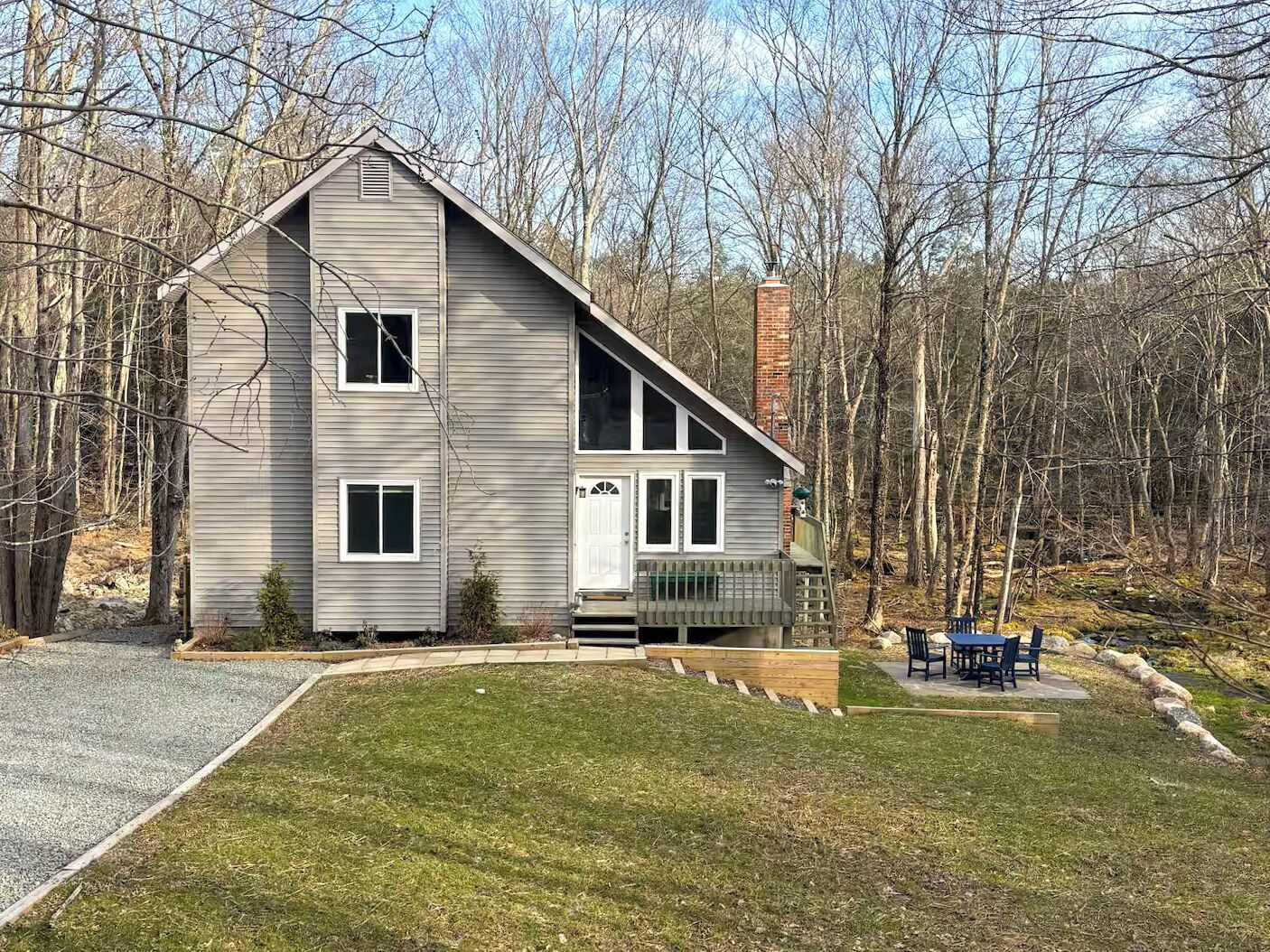 A two-story house with a front deck, surrounded by a wooded area.