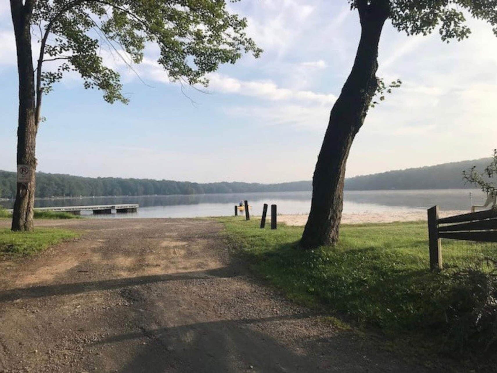 A gravel path leading to a lake with a dock, surrounded by trees and a bench.