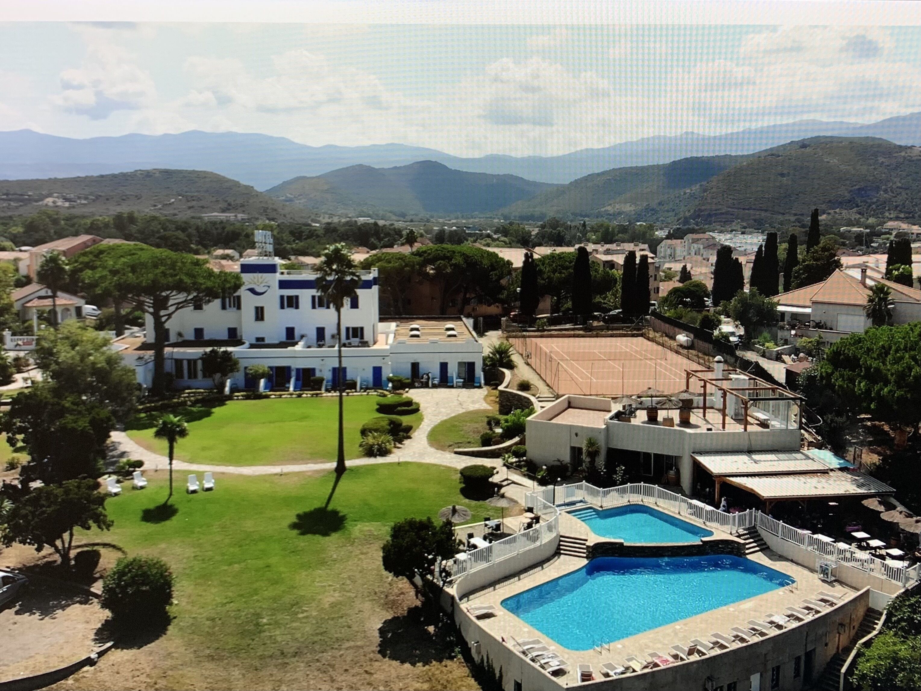 A resort with a swimming pool, tennis courts, and a large building with a blue and white facade.
