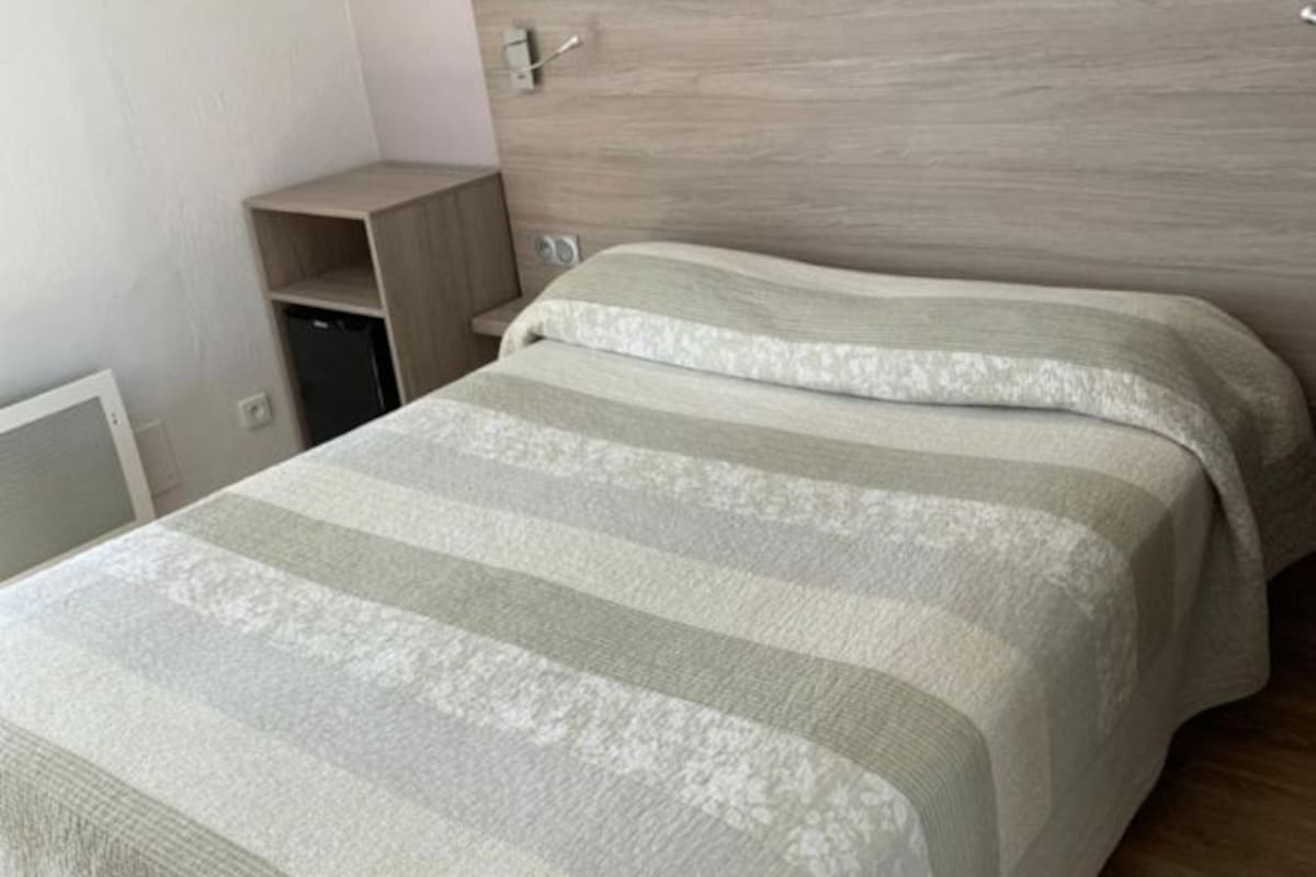Un dormitorio con cama, cabecero de madera, estante pequeño y luz empotrada en la pared.