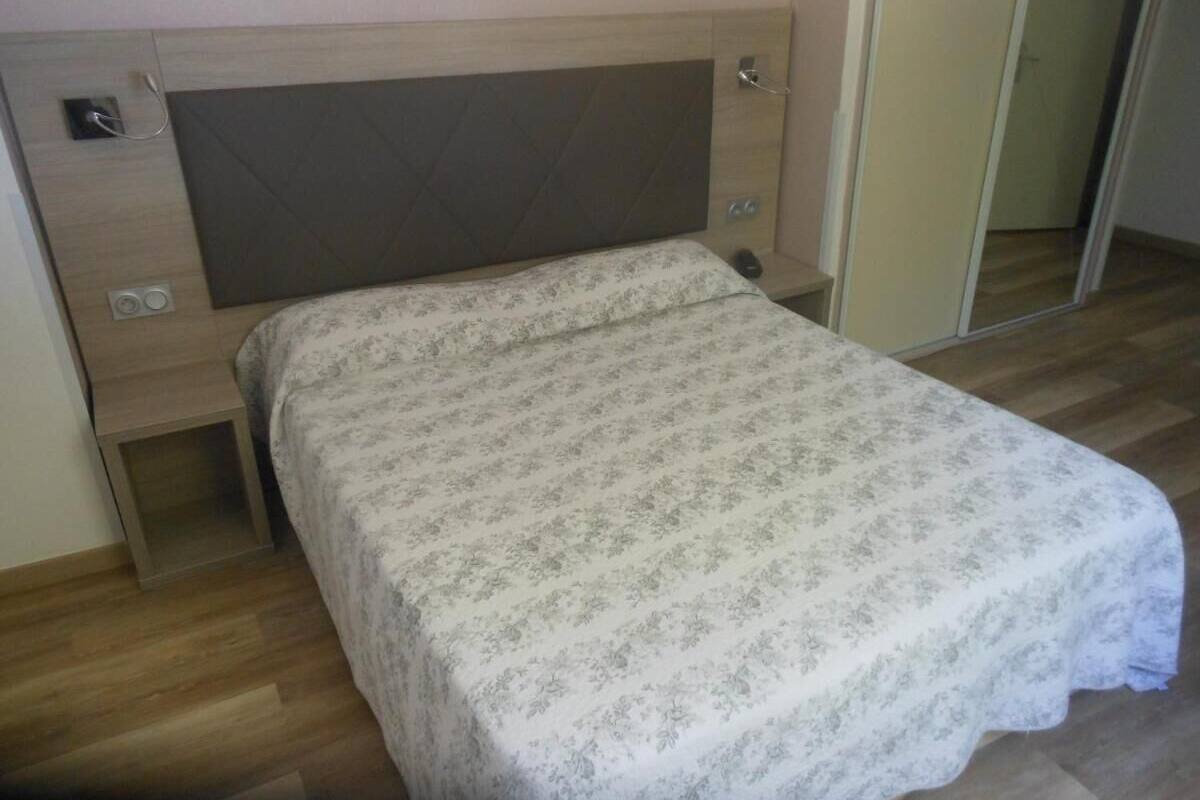 Ein Einzelbett mit einem gemusterten Bettbezug in einem Zimmer mit Holzboden und einem Kopfteil mit Stauraum.