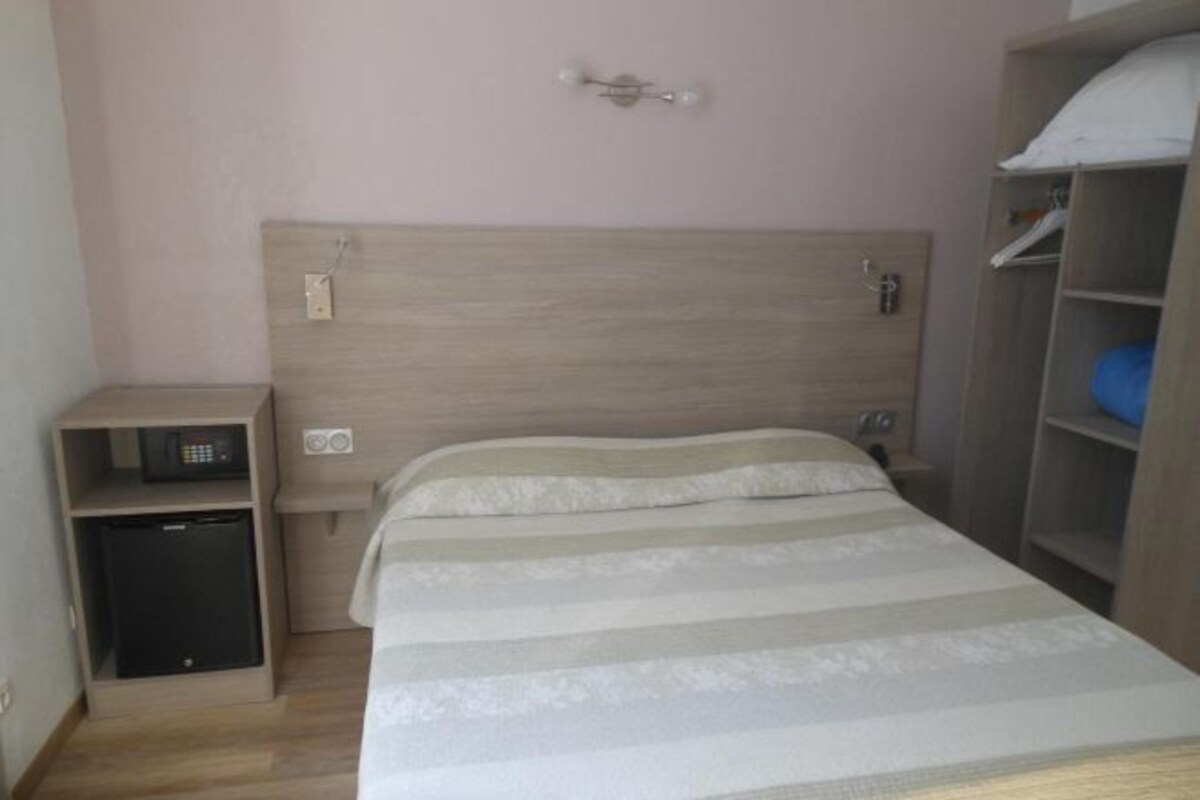 Un dormitorio con cama, una mesita de noche, un escritorio pequeño con una computadora y un armario.